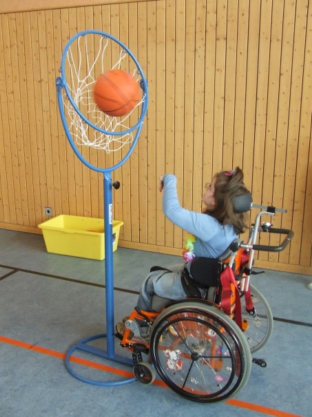 Foto einer Schülerin im Rollstuhl, die einen Ball in einen Basketballkorb wirft